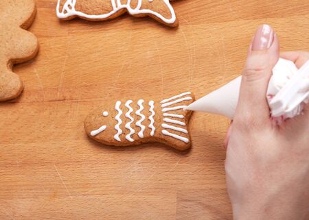 Decorating gingerbread cookies fish with white icing, selective focus and place for textの写真素材