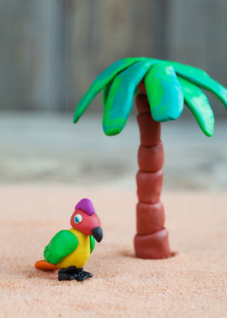 Plasticine world - little homemade multicolored parrot and palm on a wooden background, selective focus and place for textの写真素材