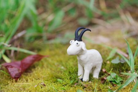 Plasticine world - little homemade white goat on green background, selective focus and place for textの写真素材