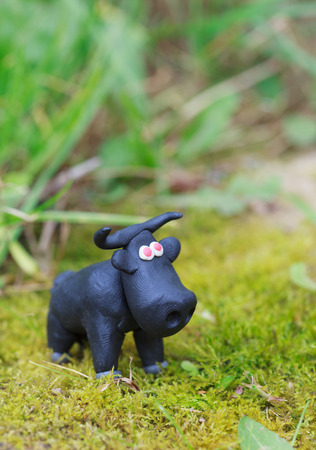 Plasticine world - little homemade black bull with red eyes on green background, selective focusの写真素材