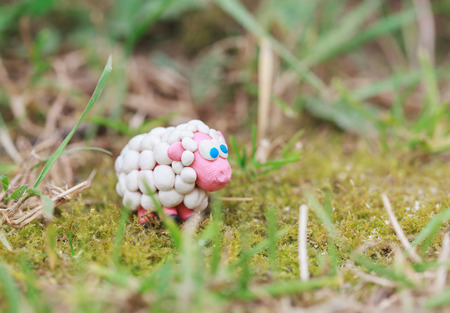 Plasticine world - little homemade white sheep with blue eyes on green background, selective focus and place for textの写真素材