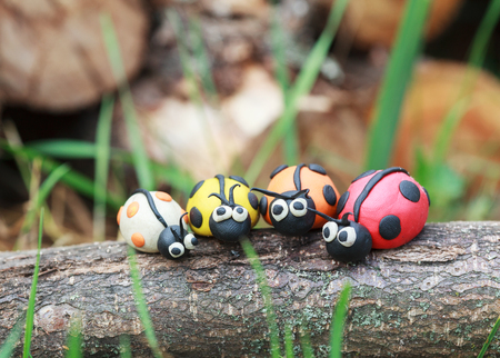 Plasticine world - four little homemade colorful ladybirds sitting on a tree trunk, selective focus on some bugsの写真素材