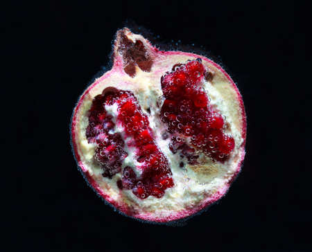 Red pomegranate in water with air bubbles on a black backgroundの写真素材