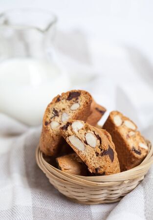 traditional Italian biscotti cookies with almonds and chocolate in basket with jar of milk, selective focusの写真素材