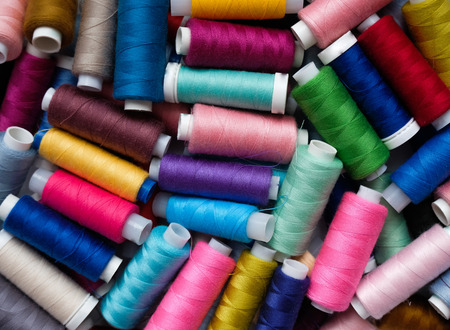 From above of messy assortment of multicolored threads on spools lying in heap