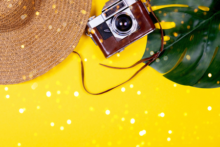 Womens traveler accessories: straw hat, tropical leaf monstera, retro camera on yellow background with bokeh lights. Concept of travel with copy space. Summer background. Flat lay, overviewの写真素材