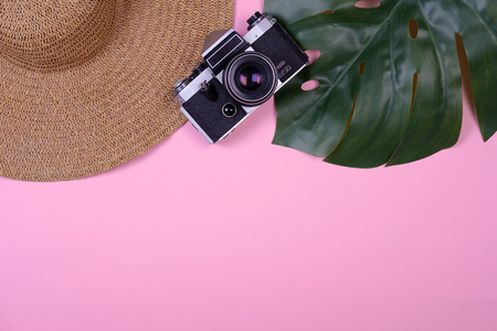 Womens traveler accessories: straw hat, tropical leaf monstera, retro camera on pink background. Concept of travel with copy space. Summer background. Flat lay, overviewの写真素材