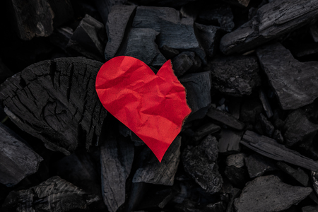 Burning red paper heart on coals minimal background. Sadness, frustration, relationship break up symbol. Color origami on smouldering beams top view backdrop. Divorce, cheating, split up conceptの写真素材