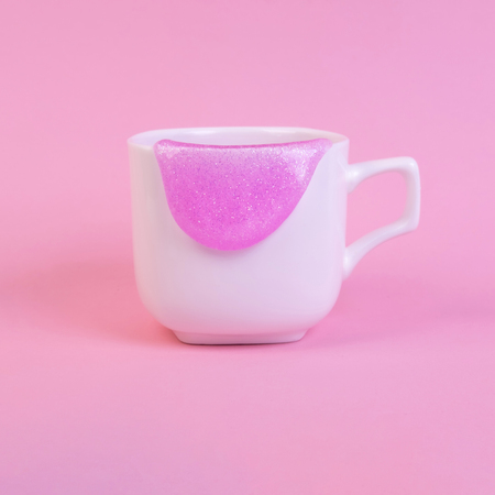 Bright pink glitter slime comes out of mug. White cup on pink background. Art neon surrealism and minimalism conceptの写真素材