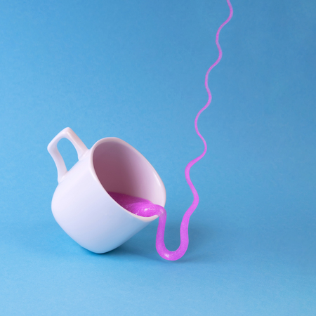 Bright pink glitter slime comes in mug. White cup on blue background. Art neon surrealism and minimalism conceptの写真素材