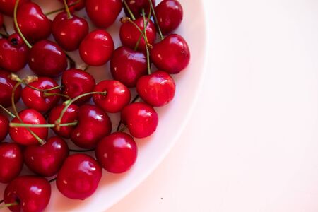 Plate with sweet cherries closeup. Freshly harvested summer berry in white bowl. Vitamin containing...