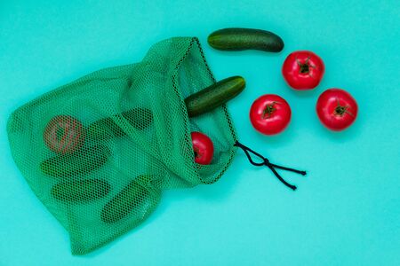 Fresh cucumbers and tomatoes falling out of shopping net. Ripe vegetables flat lay top view. Healthy vegetarian diet. Grown natural products. Salad ingredients on blue backdrop. Simple wallpaperの写真素材