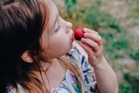 Girl eating strawberry. Child face closeup. Healthy, organic food. Fresh ripe berry. Summertime, spring sweet treat. Quick snack. Natural handpicked tasty food. Vegetarian and vegan dietの写真素材