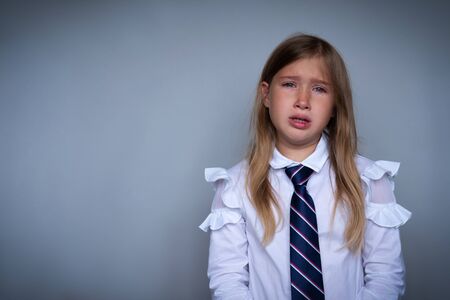 Small schoolgirl covering face, crying portrait. Preteen stressed, scared child hiding, wiping off tears. Pupil, student in school uniform. Back to school, sad, miserable young girl ready for classの写真素材