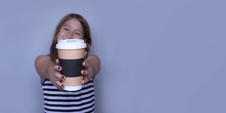 Smiling girl giving, showing coffeecup closeup side view. Drinking hot, energizing coffee to go, take away drink in disposable paper cup . Everyday routine with your child. Safe, recyclable materialsの写真素材