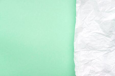 Crumpled white parchment paper on light green, turquoise background top view. Rough, wrinkled, damaged paper texture. Abstract design, creased, aged style art, wallpaper, backdrop, backgroundの写真素材