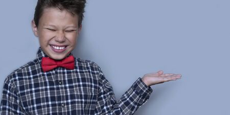 Small boy showing something with palm of hand. Nerdy schoolboy presenting school project portrait. Schoolboy with white smile, preteen child with cupped hand on grey background. Dentistry conceptの写真素材