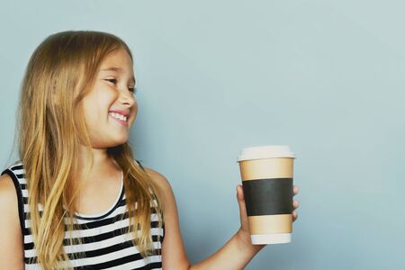 Smiling girl giving, showing coffeecup closeup side view. Drinking hot, energizing coffee to go, take away drink in disposable paper cup . Everyday routine with your child. Safe, recyclable materialsの写真素材