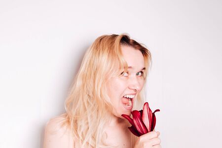 Portrait 40 years old woman with blond hair and red lily flower in mouth on light gray background with copyspaceの写真素材
