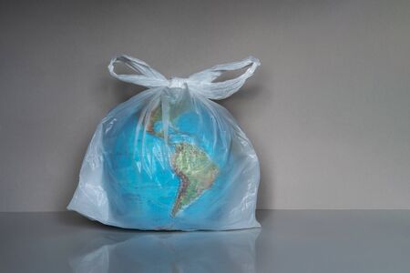 Earth globe in plastic bag on grey background. Environmental pollution and contamination problem concept. Ecology protection, waste reduce and recycle. Save planet, stop plastic ideaの写真素材