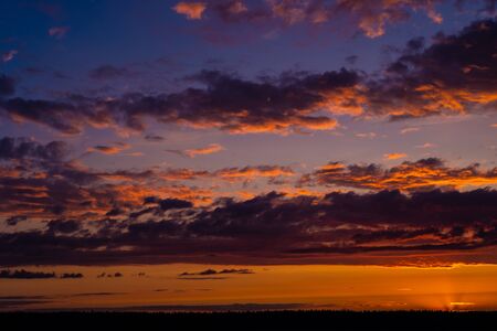 Evening sky at sunset background. Dark clouds hanging above horizon. Majestic cloudscape in blue, orange, violet shades. Grey cloudlets bringing rain. Countryside skyline in twilight timeの写真素材