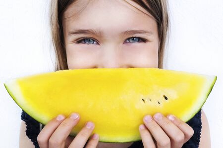 Happy girl holding watermelon slice close up. Smiling child eating yellow fruit. Healthy nutrition, organic summer product concept. Kid with cheerful facial expression. Positive emotions ideaの写真素材