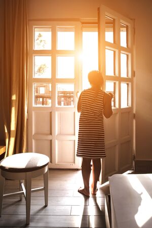 Beautiful young woman standing in doorway at sunset. Silhouette of sensual lady looking at pink sky in twilight. Girl enjoying evening scenery. Female figure in door entrance back viewの写真素材