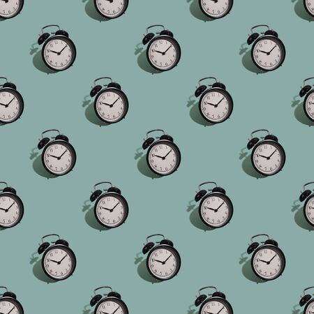 Many black classic style alarm clock with hard shadow isolated on green background. Smile time concept. Seamless patternの写真素材