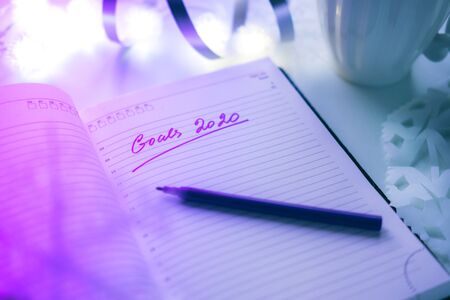2020 goals written on a diary with light, hot coffe or tea and decoration. Happy New Year and...