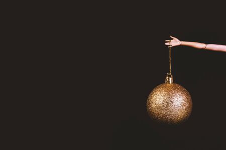 Christmas bauble on brown background. Round fir tree decoration with golden glitter, xmas ornament hanging on doll hand. Stylish new year themed backdrop with childish toys and copyspaceの写真素材