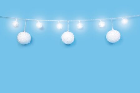 Christmas ornaments on cyan blue background. Festive decorations, white sparkling baubles and glowing lights garland. Traditional winter holiday celebration accessories. Xmas backdrop with copyspaceの写真素材