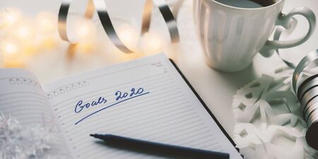 2020 goals written on a diary with light, hot coffe or tea and decoration. Happy New Year and motivation consept backgroundの写真素材