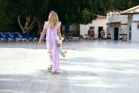 Young girl in dress with skateboard at summer sunrise. Girl walking on street. Lifestyle concept. Stock photo.の写真素材