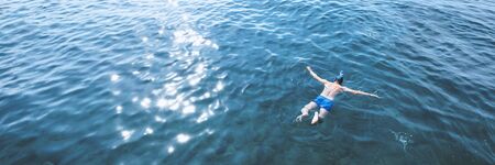 Young man in swimwear lying on blue water. Man in swimming mask relaxing in sea. Tropical summer vacation. Tranquility and peace. Person floating in ocean and watching fishの写真素材
