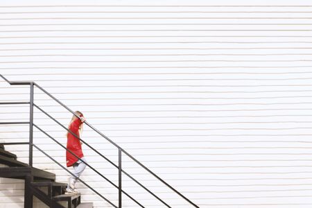 Girl with sunglasses and red jacket goes down black stairs near white wall. Spending time outdoors. Child playing outside in autumn. Childhood memories. Adventure in wilderness. Banner with copyspace.の写真素材