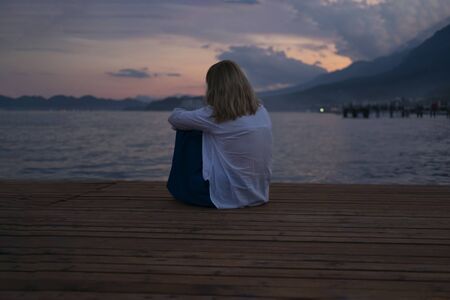 Young woman looking at sea and dreaming. Pretty lady on wooden pier near blue ocean. Thoughtful girl at sea resort. Person on holiday, enjoying summer vacationの写真素材
