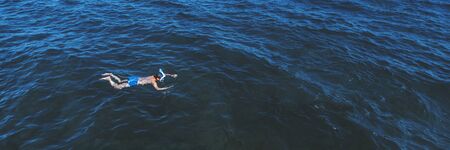Young man in swimwear lying on blue water. Man in swimming mask relaxing in sea. Tropical summer vacation. Tranquility and peace. Person floating in ocean and watching fish. Stock photo.の写真素材