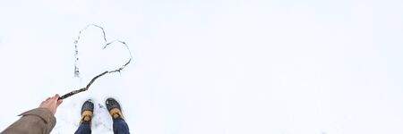 Female hand draw heart by stick on white snow. Banner of beautiful winter background for Valentines Day or Christmas with copyspace. Stock photo.の写真素材