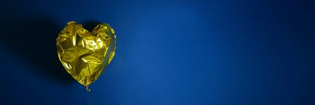 Banner of golden heart shaped air ballon on blue background. Crumpled ballon. Birthday and valentines day concept. Stock photo.の写真素材
