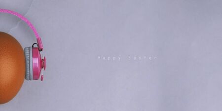 Easter egg with pink headphones on gray background with copyspace and text. Banner of macro moody...
