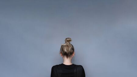 Young girl simple hairstyle back view. Depression, loneliness and quarantine concept. Fashion model, trendy woman. Blonde long hair in top bun close-up photo. Elegant and everyday look for girlsの写真素材