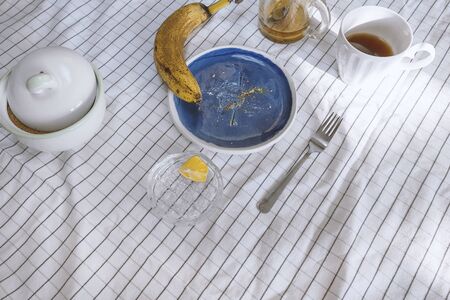 Crumbs and food object on table with blue ceramic plate and yellow banana on table with white clerical tablecloth. Stock photo.の写真素材