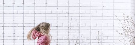 Happy girl rejoices spring. Young child playing outside. Banner of Sunny day activity with copyspace. Happy, joyful kid outdoors. Having fun alone. Beautiful landscape with white brick wall.の写真素材