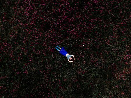 Staycation. 40 years old woman with arms and legs outstretched lying and similing on green grass in...