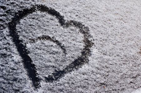A drawing in the form of a heart on the fallen snow on the car glassの写真素材