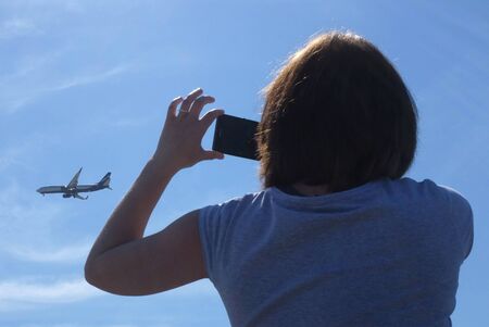 A girl is photographing a plane flying in the skyの写真素材