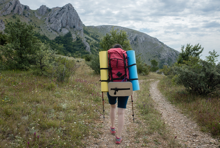 Young girl tourist with backpack walking along a mountain roadの写真素材