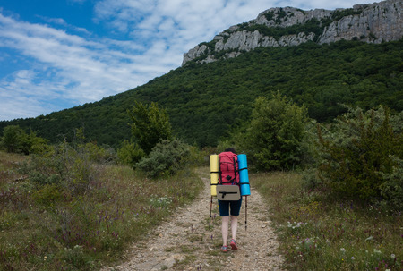 Young girl tourist with backpack walking along a mountain roadの写真素材