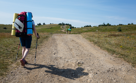 Young girl tourist with backpack walking along a mountain roadの写真素材