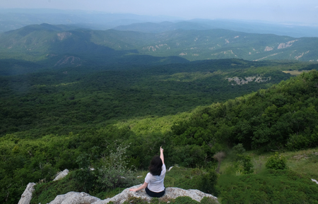 A young girl sits on edge cliff and looking at mountain landscapeの写真素材